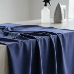 Granatowa tkanina na betonowym blacie, gotowa do dekatyzacji. Obok żelazko i spryskiwacz.