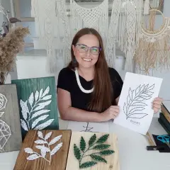 Kobieta prezentuje swoje prace string art, w tym jelenia i liście. Pokazuje też szablony do string art, które pomagają tworzyć piękne dekoracje.