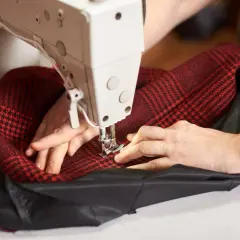 Ręce szyjące na maszynie czerwoną tkaninę w kratkę z czarną podszewką. Precyzyjne szycie to klucz do tego, jak wszyć podszewkę do płaszcza.
