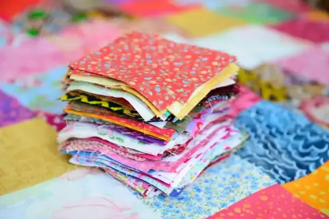 Stos kolorowych kwadratów materiałów, gotowych do stworzenia patchworku. To właśnie patchwork – sztuka łączenia skrawków tkanin w piękne wzory.